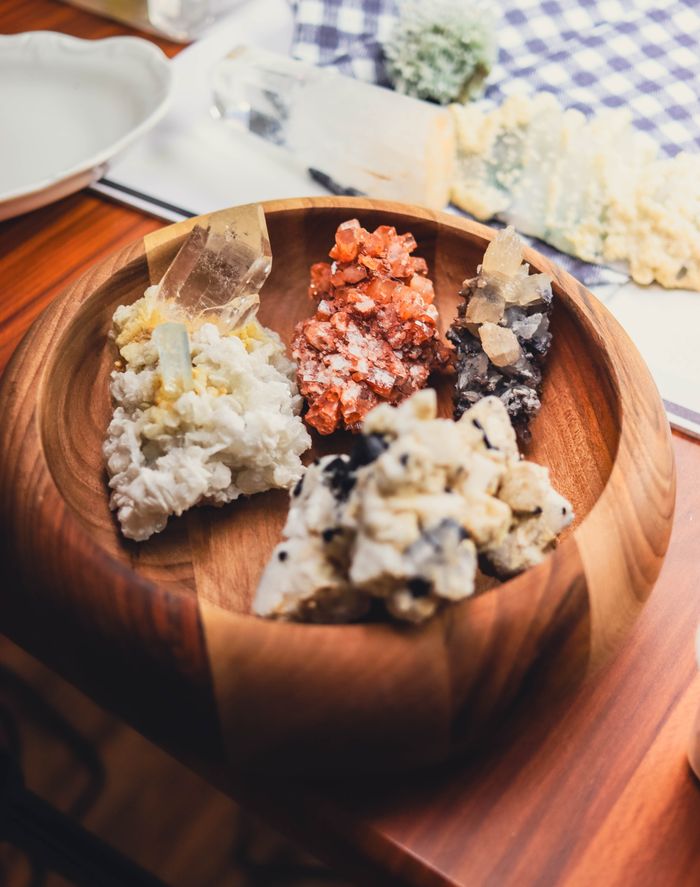 trusted-partner A variety of colorful minerals displayed in a wooden bowl on a table.